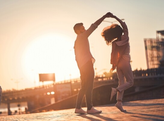 A man and woman dancing outdoors with the sunset in the background.